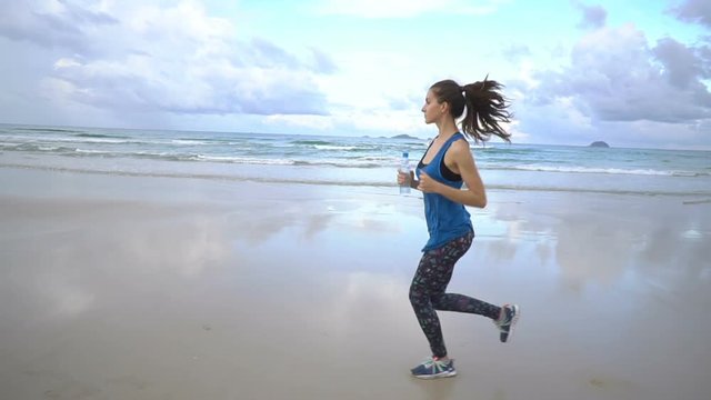Healthy active young woman running along shore line at sunrise. Female jogging