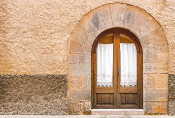 Fototapeta na wymiar Alte Holz Tür mit Glas und Gardine Stein Bogen und Mauer rustikal