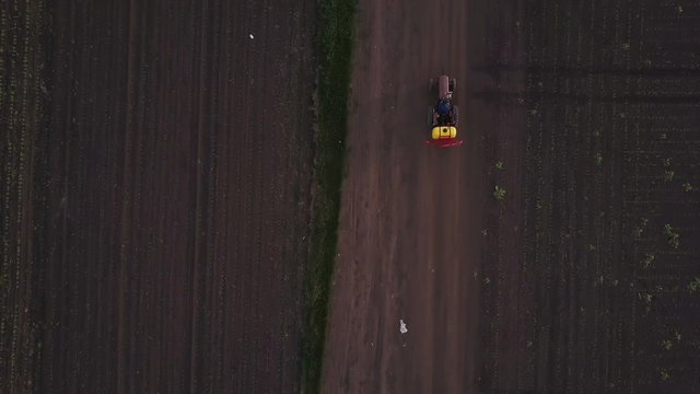 Tractor with crop sprayer on country road through wheat field, aerial view from drone pov