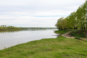A dirt road on the coast of a calm river in the evening in the spring.