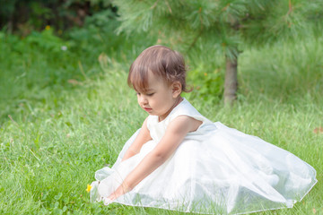 a little girl sits on green grass in a pretty dress