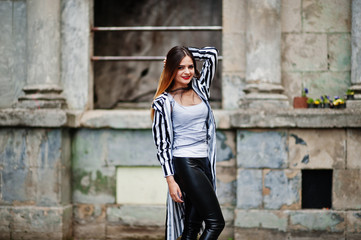 Fashionable woman look with black and white striped suit jacket, leather pants,  posing at old street. Concept of fashion girl.