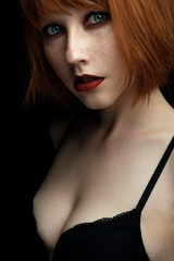 Portrait of a young girl with redhead and freckles with red lips and blue eyes with dark makeup looking at the camera