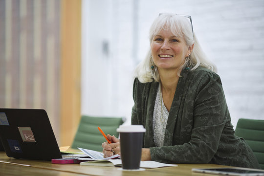 Portrait Of Smiling Businesswoman With Laptop Computer Sitting In Board Room At Office