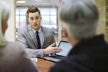 Businessman explaining to colleagues over laptop in office meeting