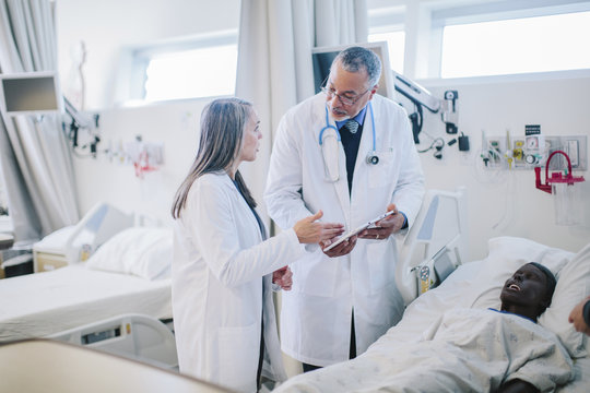 Male Doctor Discussing With Female Coworker Over Tablet Computer In Hospital Ward