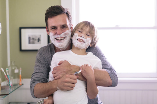 Portrait of happy father and son with shaving cream on face standing in bathroom