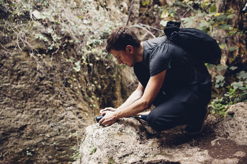 Male hiker with backpack photographing through camera while crouching on rock formation