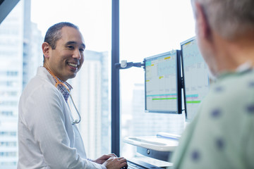 Smiling male doctor talking to patient while using computer in hospital ward