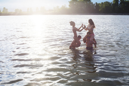 Rear view of female friends in bikini standing at riverbank on sunny day