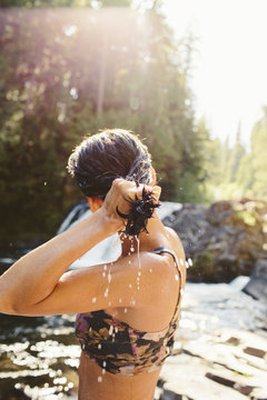 Side view of woman wringing hair while standing in forest at riverbank