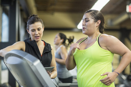 Trainer instructing woman exercising on treadmill in gym