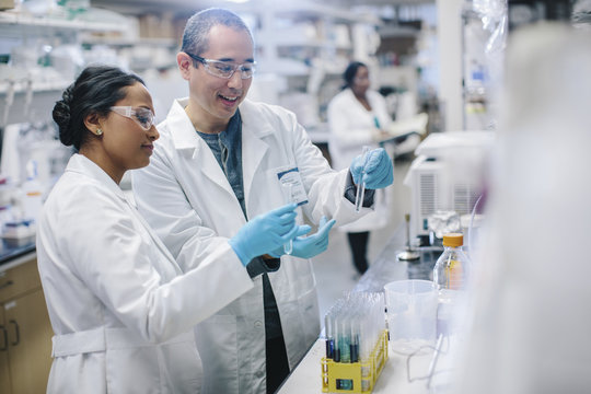 Doctors examining test tubes while coworker working in background at laboratory