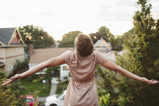 Rear view of happy woman with arms outstretched standing on rooftop against sky
