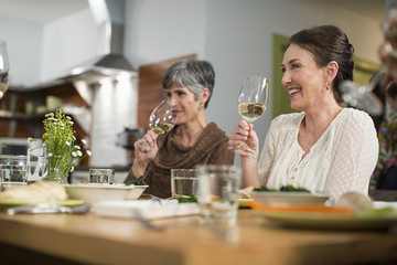 Smiling female friends drinking wine while sitting at table during social gathering