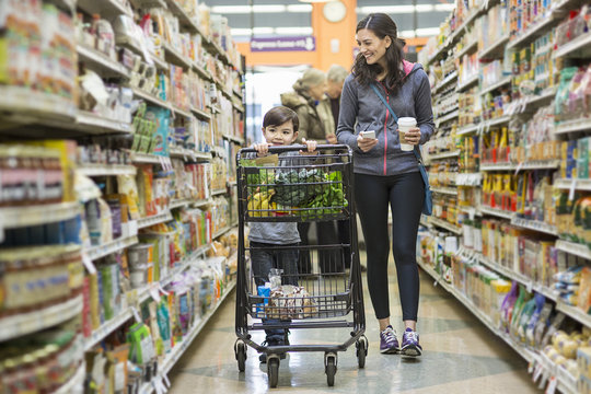 Woman walking by son pushing shopping cart at supermarket