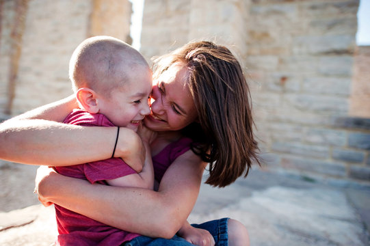 Happy Mother Embracing Son While Sitting By Wall