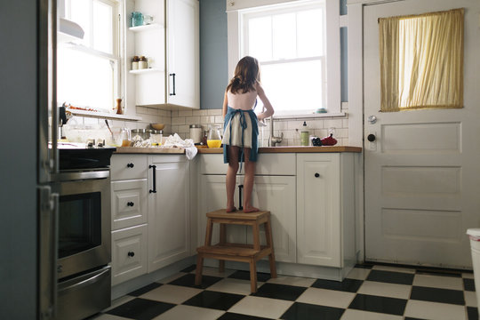 Rear View Of Girl Washing Dish In Kitchen At Home