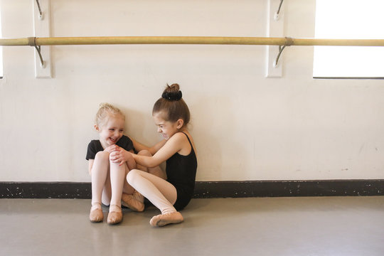 Playful girl tickling friend while sitting in ballet studio