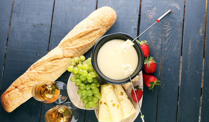 Gourmet Swiss fondue dinner with assorted cheeses on a board and strawberries alongside a heated...