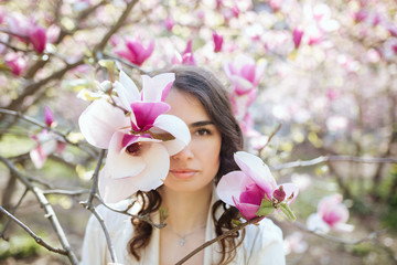 Naklejka premium Beauty woman standing on Magnolia blossoming flowers background.