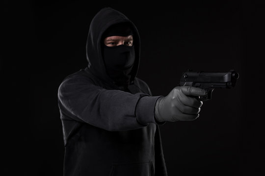 The robber in a mask with a gun pointed to the side on a black background