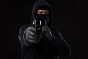 Masked robber with gun aiming into the camera against a black background