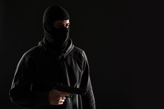 The robber in a mask with a gun pointed to the side on a black background
