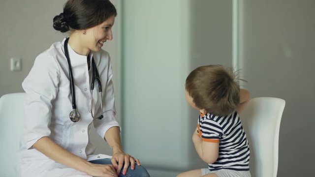 Young woman doctor talking little boy and listening with stethoscope in medical office