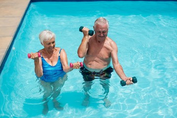 Senior couple exercising with dumbbells in the pool