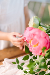 Fototapeta na wymiar wedding, childcare, floral design, celebration, decoration concept - little soft hand of girl in white dress touching grand blooming bud of peony sorrounded by green leaves