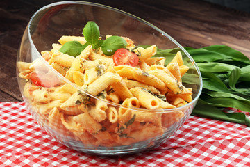 Penne pasta in tomato sauce with chicken, tomatoes decorated with basil on a wooden table