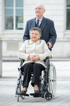 senior man pushes his disabled wife through the city