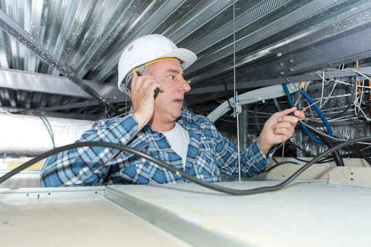 electrician on the phone with client inside ceiling