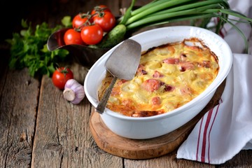 Potato casserole with sausages, onions and cheese on an old wooden background. Rustic style.