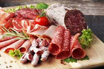 Food tray with delicious salami, pieces of sliced ham, sausage, tomatoes, salad and vegetable -...