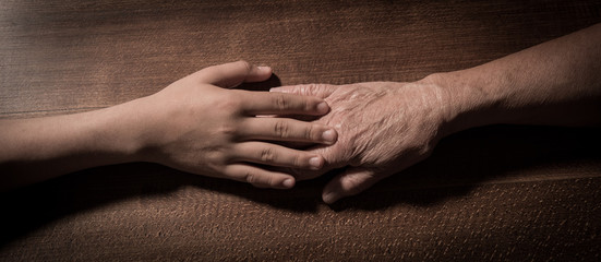 Child hands holding senior woman's hands on brown background