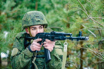 Portrait of a Russian soldier in modern military uniforms and weapons, machine gun. Green form on the background of a pine forest