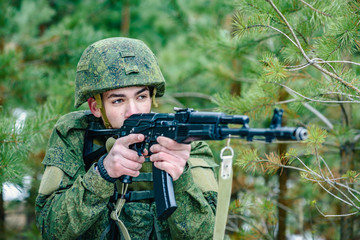 Fototapeta premium Portrait of a Russian soldier in modern military uniforms and weapons, machine gun. Green form on the background of a pine forest