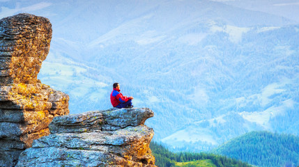 Man meditating in lotus pose upon the cliff in the mountains. Yoga and tourism lifestyle.
