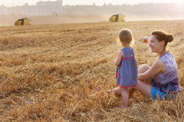 Naklejka na ściany i meble Happy family: a young beautiful woman with her little cute daughter, sit in the orange field on a sunny summer day. Parents and kids relationship.