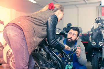 young male worker assisting female customer in repairing motorcycle in workshop