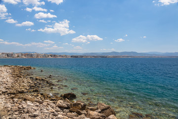 Coast landscape with stony beach, city and blue sea