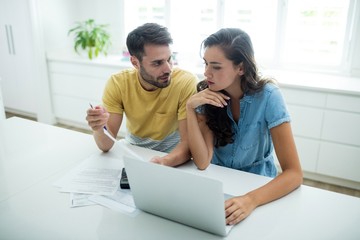 Worried couple calculating their bills with laptop