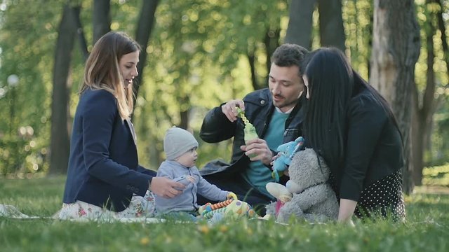 Swedish family with little son relaxing on coverlet in park