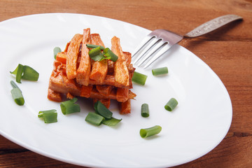 Baked carrots with green onions on a white plate. Organic Vegetarian Food on wooden background