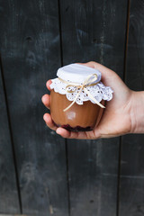 Creamy dessert in a small glass jar with decoration and ribbon which held in hand on a dark background