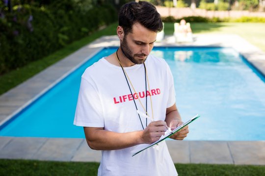 Lifeguard writing on clipboard at poolside