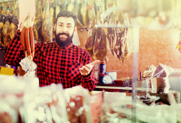 Young male customer examining sausages in butcher’s shop