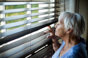 Senior woman looking out from window blind